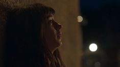 a woman with long hair standing next to a wall in the dark, looking off into the distance