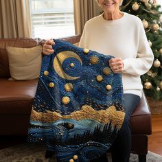 an older woman is holding up a piece of art in front of a christmas tree