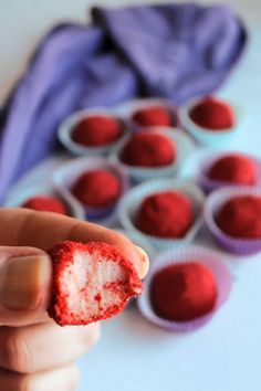 a hand holding a half eaten strawberry cupcake in front of muffin tins