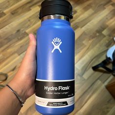 a hand holding a blue hydro flask on top of a hard wood floored floor