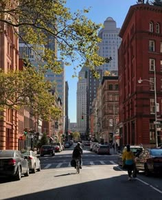 two people riding bikes down the street in front of tall buildings and parked cars on both sides