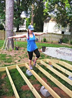 a woman in blue shirt and black shorts standing on top of a wooden deck next to a tree