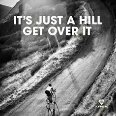 a man riding a bike down a dirt road next to a lush green hillside with the words it's just a hill get over it