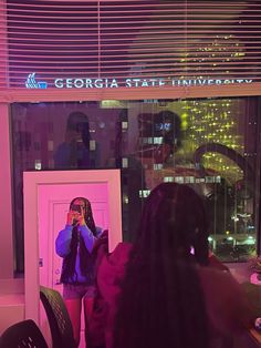 a woman taking a selfie in front of a door with the city lights behind her