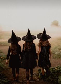 three girls wearing witches hats walking down a dirt road