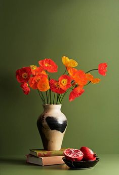 a vase filled with red and yellow flowers next to a bowl of pomegranates