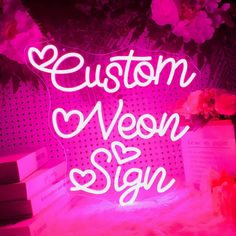 a neon sign that says custom neon signs on the side of a table with flowers and books