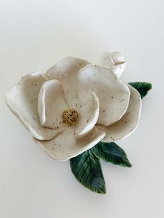 a white ceramic flower with green leaves on a white tableclothed surface, ready to be used as an ornament