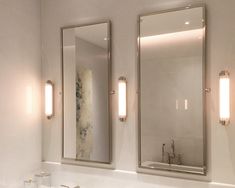 a bathroom with two sinks and mirrors on the wall, one is illuminated by three lights