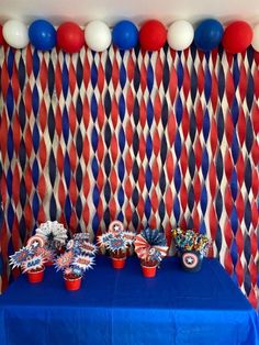 a blue table topped with red, white and blue cupcakes next to balloons