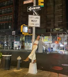 a woman standing on top of a white pole next to a street sign at night