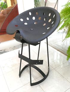 a black chair with holes on it sitting in front of a window and potted plant