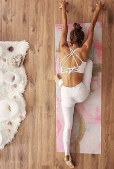 a woman in white is doing yoga on a pink mat with her arms raised up