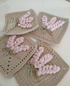 four crocheted coasters with pink flowers on them sitting on a white table