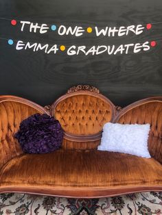 a couch with pillows on it in front of a chalkboard that says the one where emana graduates