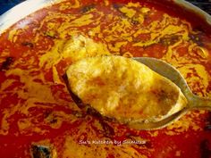 a spoon full of food sitting on top of a pan filled with red sauce and cheese