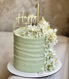 a green cake with white flowers on top and a happy birthday sign in the middle