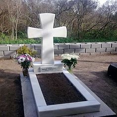 a white cross sitting on top of a cement slab next to flowers and trees in the background