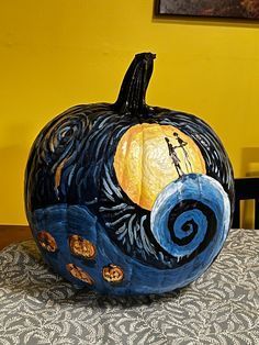 a painted pumpkin sitting on top of a table next to a wall with a painting