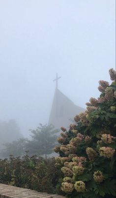 a cross on top of a steeple with flowers in the foreground and fog in the background