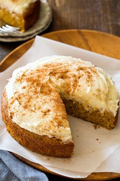 a piece of cake with white frosting sitting on top of a wooden plate next to a fork