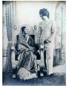 an old black and white photo of two people standing next to each other on a chair