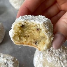 a hand holding a powdered sugar doughnut in it's middle, with the bite taken out