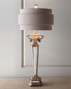 a table lamp with a white shade on it and a gold finish frame around the base