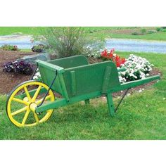 a green wheelbarrow with yellow spokes and flowers in the grass near a road