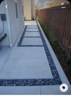 a walkway made out of stones and gravel next to a building with a fence in the background