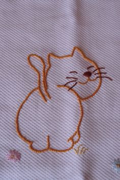 a cat embroidered onto a white sheet with flowers around it and an orange outline on the side