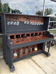 an old piano is sitting outside in front of a glass window with wine glasses on it