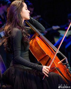 a woman with long hair sitting in front of an instrument and playing the cello on stage