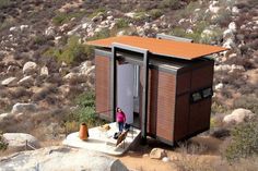 a woman standing in the doorway of a tiny house on top of a hill with rocks