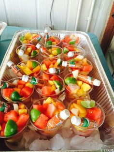 there are many small cups with fruit in them on the trays and ice cubes next to each other