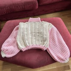 a pink and white sweater sitting on top of a red chair next to a couch