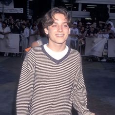 a young man standing in front of a crowd with his hand on his hip and smiling at the camera