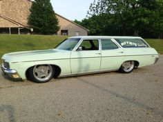 a mint green station wagon parked in a parking lot next to some trees and grass