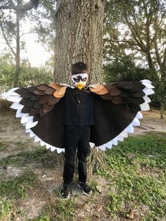 a young boy wearing an owl costume standing in front of a tree with his face painted white and brown