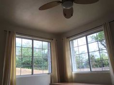 an empty room with two windows and a ceiling fan