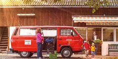 a red van parked in front of a wooden building with people standing around and talking on the phone