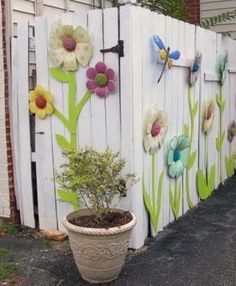 a potted plant sitting next to a white fence with flowers painted on the side