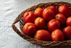 a basket filled with lots of red tomatoes on top of a white cloth covered table