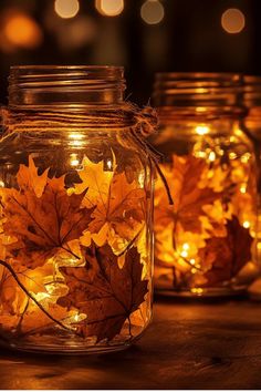 three mason jars filled with autumn leaves lit by fairy lights on a wooden table in the dark