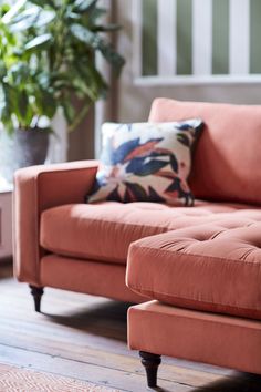 an orange couch and ottoman in a living room with a potted plant behind it