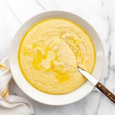 a white bowl filled with yellow liquid on top of a marble counter next to a wooden spoon