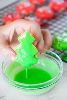 a person is dipping green paint into a bowl with a small christmas tree on it