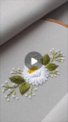 a white flower with green leaves is embroidered onto a piece of fabric on the table