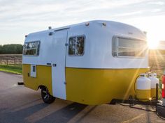 a yellow and white camper trailer parked on the side of a road next to a field