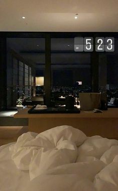 an unmade bed in front of a large window with the city lights lit up